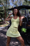 Woman in a yellow tennis outfit holding a racket and tennis balls outdoors.