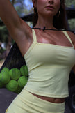 Woman in a yellow top holding a green bag of tennis balls.