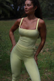Woman wearing a light yellow athletic outfit standing outdoors with greenery in the background