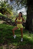 Woman in yellow athletic wear exercising outdoors in a park.
