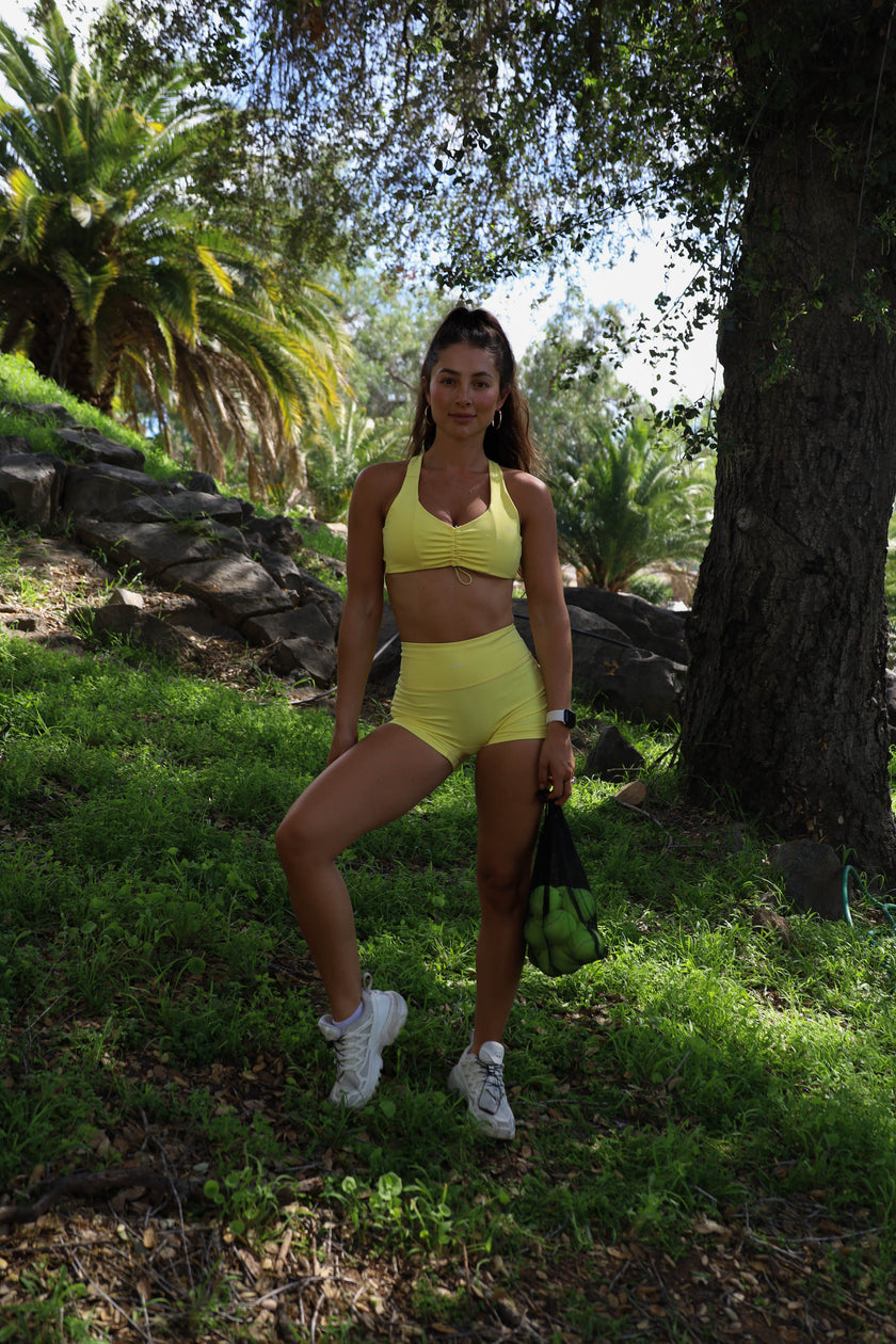 Woman in yellow athletic wear standing in a natural setting with trees and grass.