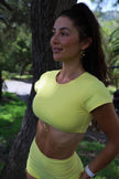 Woman in a bright yellow athletic outfit standing outdoors near a tree