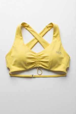 Yellow sports bra with criss-cross straps on a light gray background