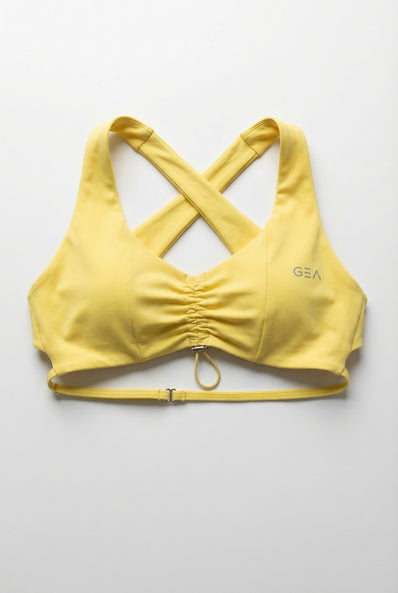 Yellow sports bra with criss-cross straps on a light gray background