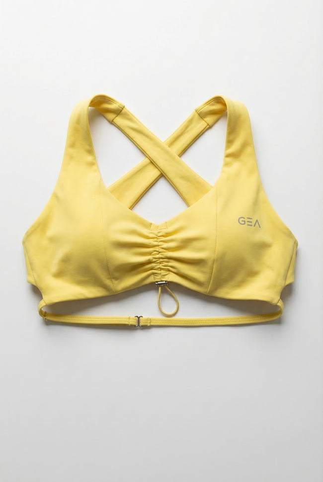 Yellow sports bra with criss-cross straps on a light gray background